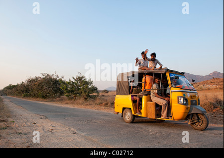 Indian auto rickshaw piena di gente, con i passeggeri seduti sul tetto, percorrendo una strada di campagna. Andhra Pradesh, India Foto Stock