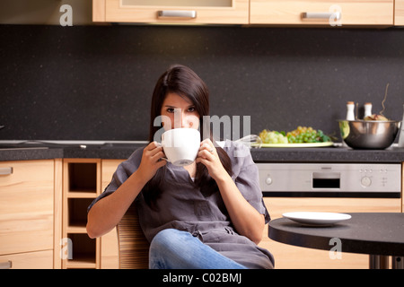 Giovane donna seduta in cucina e di bere il caffè Foto Stock