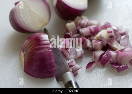 Tritare le cipolle rosse su un bianco tagliere. Foto Stock