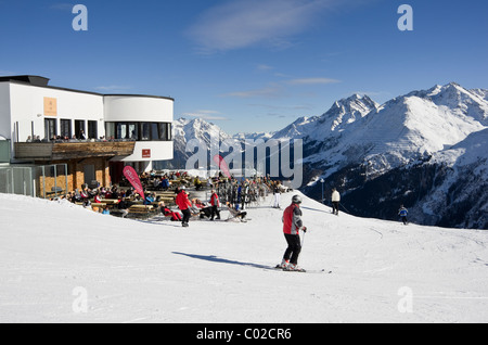 St Anton am Arleberg, Tirolo, Austria. Gli sciatori sulle piste da Galzig gondola stazione di vertice con la gente a prendere il sole fuori del ristorante Foto Stock