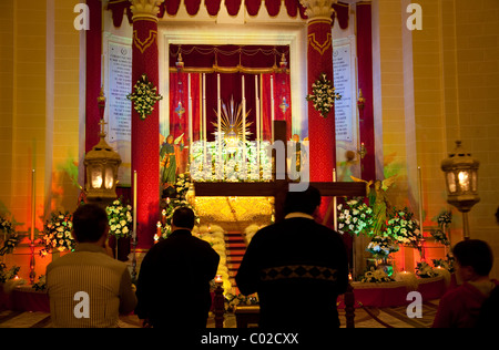 Tutto il popolo a pregare presso il sepolcro o un tabernacolo di una chiesa parrocchiale in un custom tenute in tutta Malta alla vigilia del Venerdì Santo. Foto Stock