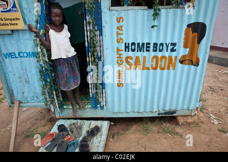 Una ragazza sta al di fuori di un taglio di capelli salon in Amuria, Uganda, Africa orientale. Foto Stock