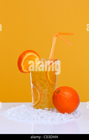 Foto di succo d'arancia fresco in un bicchiere con ghiaccio tritato, su uno sfondo arancione. Foto Stock