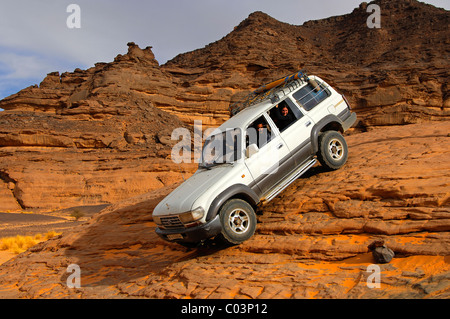 Veicolo fuoristrada con i turisti a bordo in attraversamento di una ripida roccia passaggio, Acacus, il deserto del Sahara, Libia Foto Stock