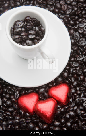 White tazza da caffè con nero, chicchi di caffè tostati e tre a forma di cuore i dolci. Foto Stock