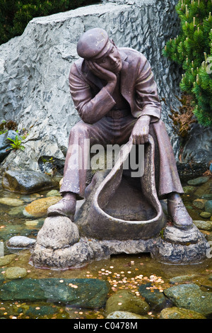 Statua di un uomo con un sacco aperto, seduto su una roccia Foto Stock