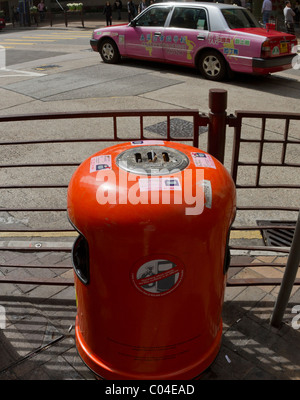 Orange cassonetto su un angolo di strada in Hong Kong con un dipinto luminosamente taxi in background Foto Stock