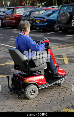 Mobilità utente scooter in sella a una di tre ruote alimentato a batteria della macchina attraverso un area parcheggio per auto Foto Stock