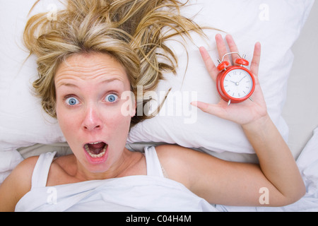 Donna nel letto di rendersi conto che ella ha dormito nonostante la presenza di una sveglia Foto Stock