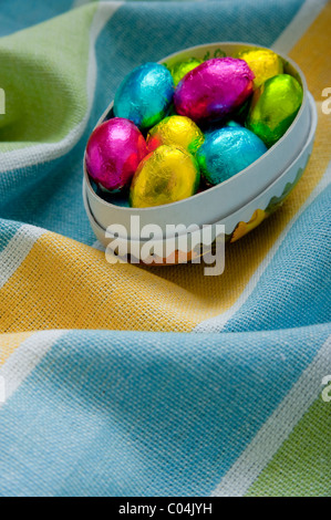 Mini uova di pasqua di cioccolato in cartone uovo scatola su textured stropicciata giallo e blu tovaglia Foto Stock