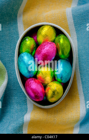 Mini uova di pasqua di cioccolato in cartone uovo scatola su textured stropicciata giallo e blu tovaglia Foto Stock