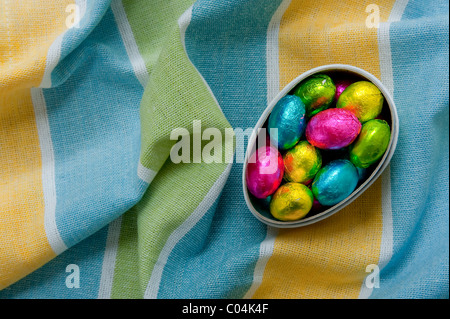 Mini uova di pasqua di cioccolato in cartone uovo scatola su textured stropicciata giallo e blu tovaglia Foto Stock