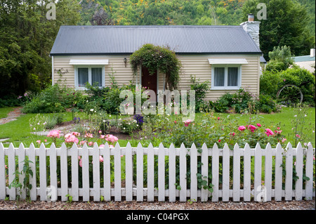 Un semplice meteo imbarcati bungalow con giardino di rose e white Picket Fence a Arrowtown, Nuova Zelanda Foto Stock