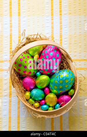 Gruppo delle colorate uova di pasqua di cioccolato di varie dimensioni in un cesto su una tovaglia Foto Stock