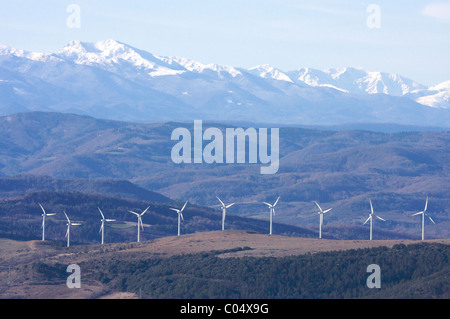 Fila di dieci wind-turbine sulle colline in anticipo delle montagne coperte di neve dei Pirenei, fattoria del vento nel sud della Francia Foto Stock