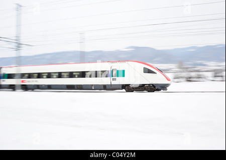 Un treno svizzero accelerando attraverso un paesaggio innevato a metà inverno. Motion Blur utilizzato per dare il senso della velocità. Foto Stock