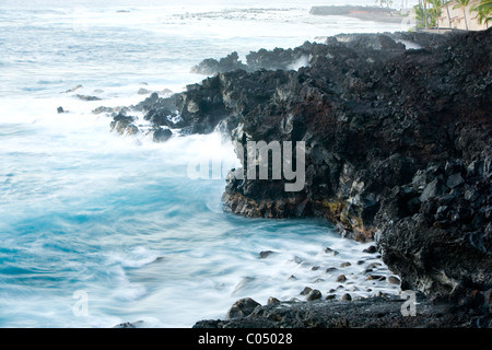 Il tempo di esposizione di surf di tornitura contro rocce laviche in Kailua Kona Foto Stock