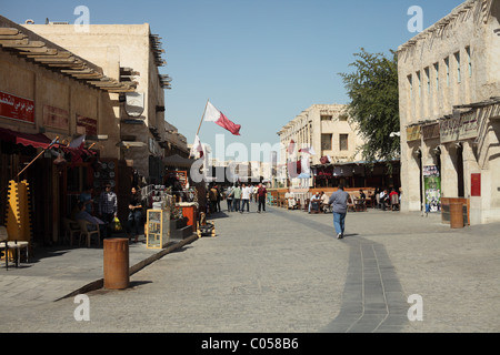 Tipica scena del pomeriggio nel Souq Waqif, Qatar, con bandiere e i visitatori locali e vagare attraverso l'ampia strada transitabile Foto Stock