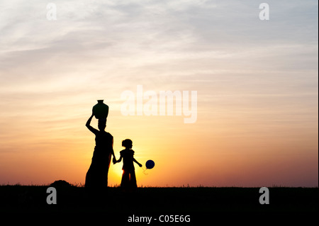 Madre indiana portando acqua pot holding childs mano con palloncino in campagna indiana. Silhouette Foto Stock