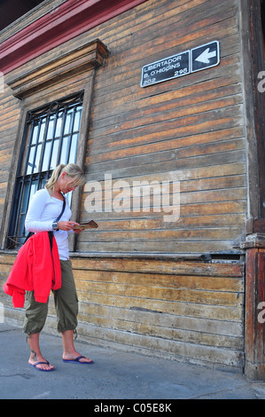 Bella turista con mappa in piedi dal vecchio edificio in legno con lo spagnolo strada segno Foto Stock