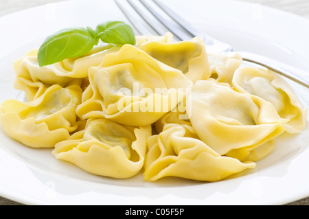 Tortellini bollito con basilico come primo piano su una piastra bianca Foto Stock