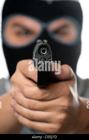 Un arrabbiato cerca uomo che indossa una maschera da sci puntando una pistola nera al visualizzatore. Funziona alla grande per il crimine o home i concetti di sicurezza. Foto Stock
