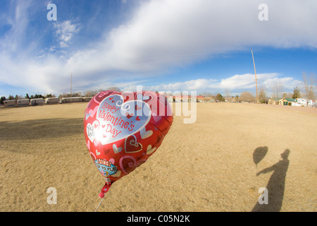 Ombra di persona in possesso di un il giorno di San Valentino a forma di cuore sul palloncino un campo vuoto. Foto Stock