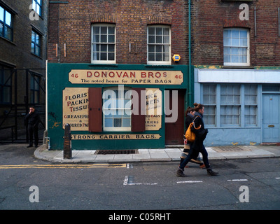Due giovani donne a piedi passato Donovan Bros sacchetto di carta shop in Spitalfields East London REGNO UNITO KATHY DEWITT Foto Stock