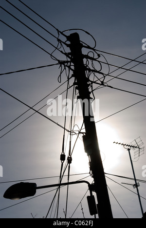 Un "telegrafo polo' con molte utilità di overhead di cavi di alimentazione o i fili su di essa, contro un cielo chiaro. Il sole è dietro la pole. Foto Stock