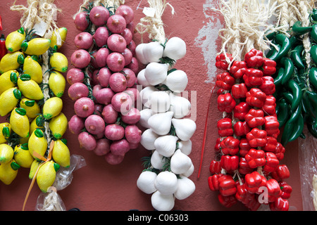 Limoni appena raccolti, cipolle, aglio, peperoni rossi e peperoni verdi appesi alla vite, in vendita all'esterno di un negozio in Italia. Un display a colori. Foto Stock