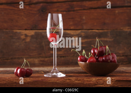 Un bicchiere di Kirschwasser, ciliegia schnapps, con ciliegie nella parte anteriore del legno rustico Foto Stock