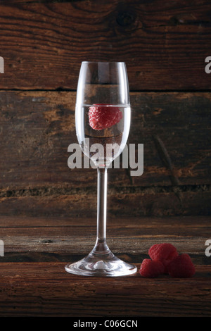 Un bicchiere di Himbeergeist, un lampone schnaps, con lamponi nella parte anteriore del legno rustico Foto Stock