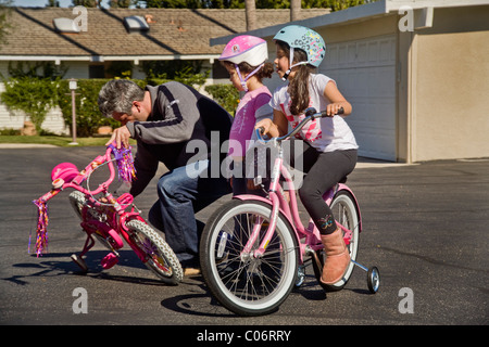 Papà regola la formazione di ruote di sua figlia di cinque anni la bicicletta come lei impara a guidare con la sorella in California. Foto Stock