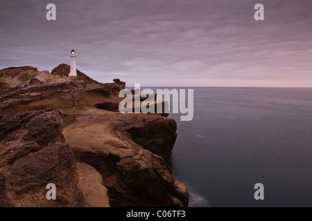 Faro appollaiato sulla roccia sopra un mare scuro. Il faro è vicino al villaggio di Castlepoint in Nuova Zelanda. Foto Stock