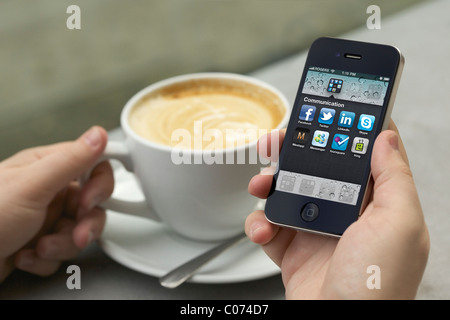 Man mano che tiene un iPhone 4 che mostra l'applicazione di social networking a uno schermo a una cafe Foto Stock