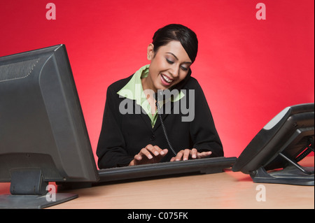 Imprenditrice utilizzando un PC desktop durante la conversazione su un telefono di rete fissa Foto Stock