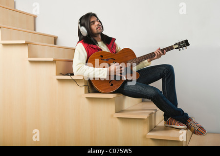 Uomo che ascolta un lettore MP3 durante la riproduzione di una chitarra su una scala Foto Stock