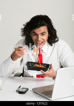 Imprenditore mangiare tagliatelle alla scrivania Foto Stock