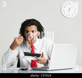 Imprenditore mangiare tagliatelle alla scrivania Foto Stock