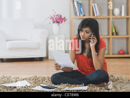 Donna di smistamento di bollette, mentre a parlare su un telefono mobile Foto Stock