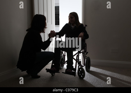 Donna consolante di una giovane donna seduta su una sedia a rotelle, tenendo le mani. Foto Stock