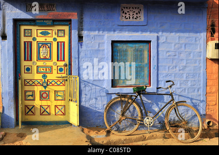 Sportello anteriore decorata con ornamenti e una bicicletta di fronte ad una parete blu in un villaggio indiano, il Deserto di Thar, Rajasthan, India Foto Stock