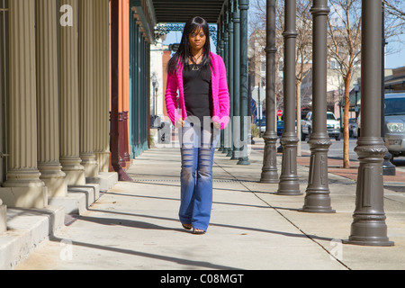 African American donna cammina verso il basso una città marciapiede in un area del centro cittadino di indossare un colore luminoso maglione. Foto Stock