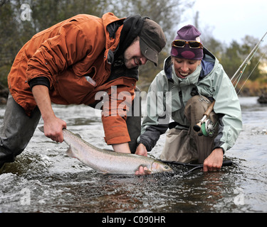 L uomo e la donna in ginocchio in acqua per mostrare una Steelhead selvatici catturati in Deep Creek, Penisola di Kenai, centromeridionale Alaska, Autunno Foto Stock