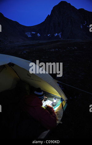 La donna in una tenda al crepuscolo consulta un gps e mappa mentre campeggio Al Lago di coniglio, Chugach State Park, centromeridionale Alaska, Autunno Foto Stock