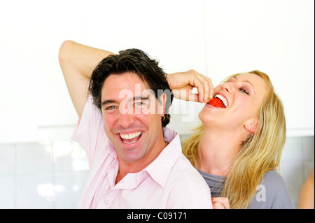 Donna di mordere in una fragola che è tenuto fuori dal suo partner Foto Stock