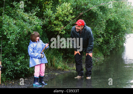 Nonno incoraggia la nipotina come ella battaglie un rosa salmone in Ingram Creek off la Seward Highway, centromeridionale Alaska Foto Stock