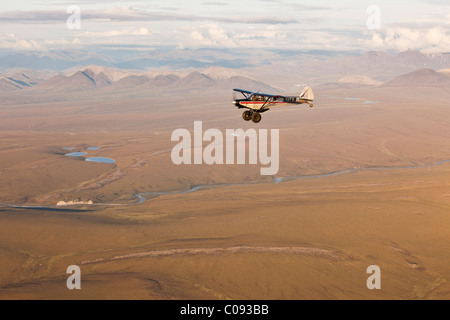 Vista aerea di un Piper Super Cub aereo volare sopra il fiume Jago con il Romanzof montagne sullo sfondo, ANWR Alaska Foto Stock