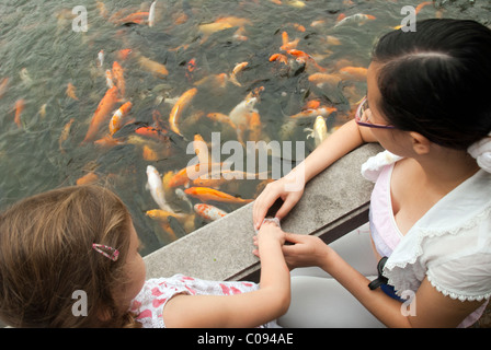 Ragazza di colore bianco e la donna cinese alimentazione di carpe koi nel Parco QiFeng Foto Stock