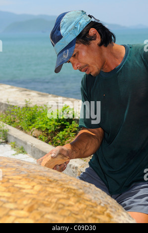 Pescatore riparando il suo tradizionale appuntamento barca di vimini, Vietnam, sud-est asiatico Foto Stock